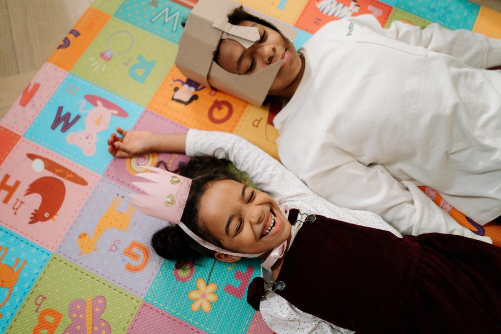 Two children playing as knight and princess while lying on an alphabet mat. 